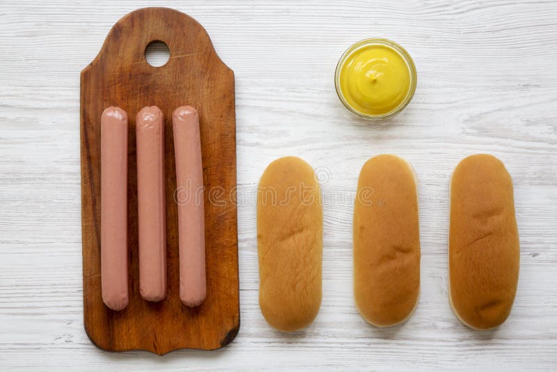 Ingredientes para fazer cachorros quentes: salsichas na placa de madeira, nos bolos de cachorro quente e na mostarda no fundo de imagens de stock royalty free Ingredientes para fazer cachorros quentes: salsichas na placa de madeira, nos bolos de cachorro quente e na mostarda no fundo de imagens de stock royalty free
