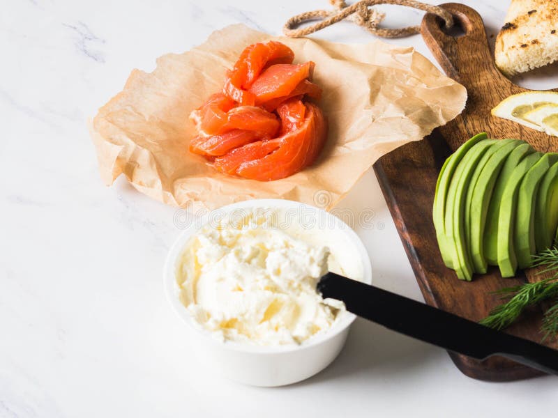 Ingredientes para sanduíches da preparação com queijo creme, salmão, abacate em brindes grelhados no fundo de mármore branco Copi fotos de stock Ingredientes para sanduíches da preparação com queijo creme, salmão, abacate em brindes grelhados no fundo de mármore branco Copi fotos de stock
