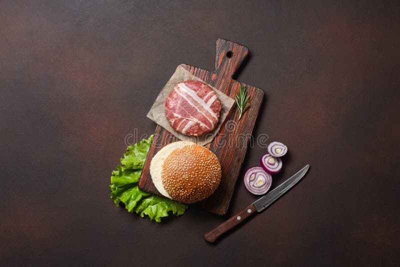 Ingredienti cotoletta, pomodori, lattuga, panino, formaggio, cetrioli e cipolla crudi dell'hamburger su fondo arrugginito fotografia stock Ingredienti cotoletta, pomodori, lattuga, panino, formaggio, cetrioli e cipolla crudi dell'hamburger su fondo arrugginito fotografia stock