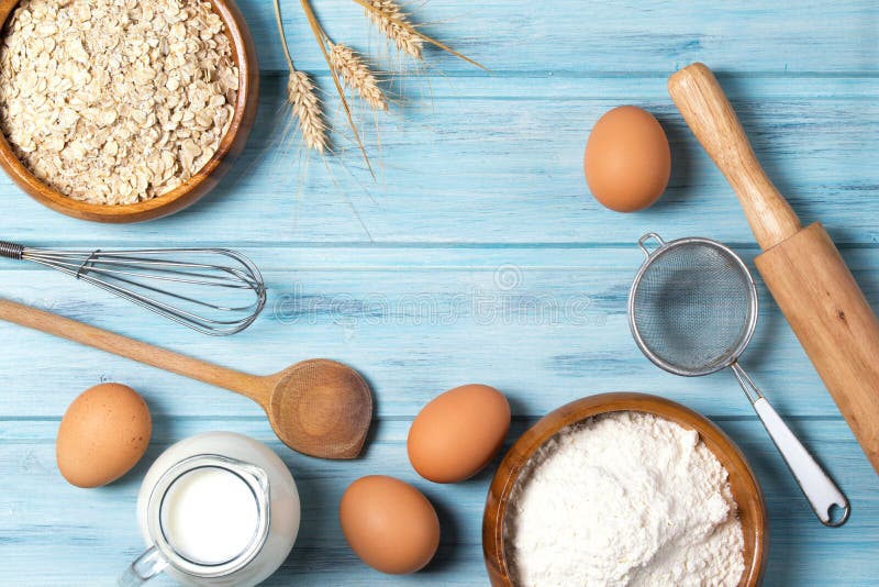 Ingredients for baking, milk, eggs, wheat flour, oats and kitchenware on light blue wooden background, top view. Ingredients for baking, milk, eggs, wheat flour, oats and kitchenware on light blue wooden background, top view