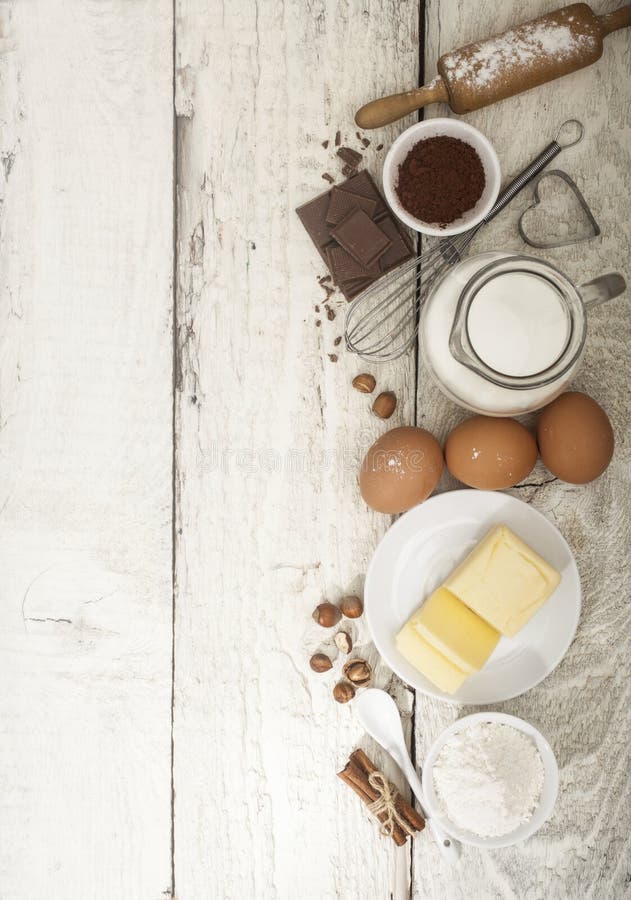 Ingredients for the preparation of bakery products: flour eggs butter milk chocolate cocoa nuts. Top view. Rustic style. White wooden background. Ingredients for the preparation of bakery products: flour eggs butter milk chocolate cocoa nuts. Top view. Rustic style. White wooden background.