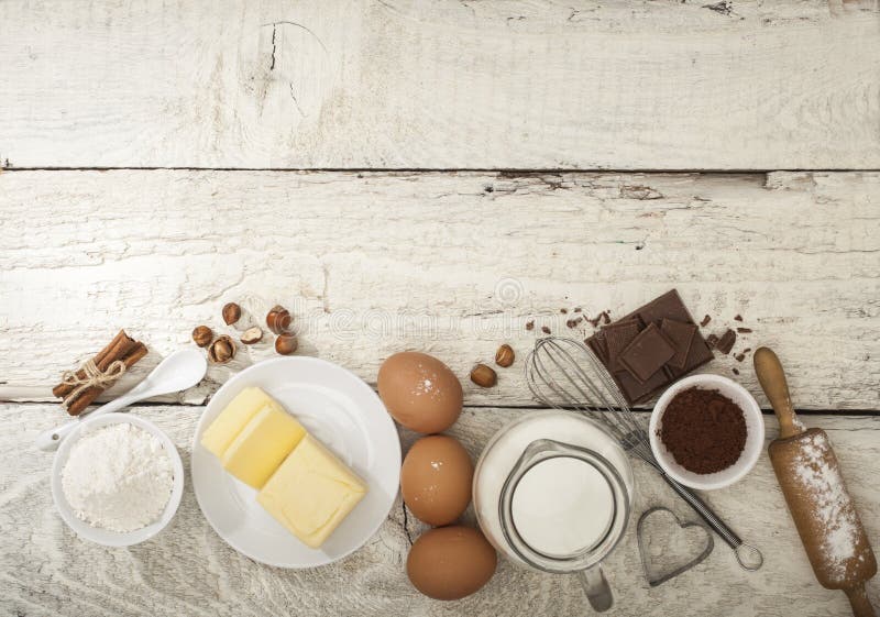 Ingredients for the preparation of bakery products: flour eggs butter milk chocolate cocoa nuts. Top view. Rustic style. White wooden background. Ingredients for the preparation of bakery products: flour eggs butter milk chocolate cocoa nuts. Top view. Rustic style. White wooden background.