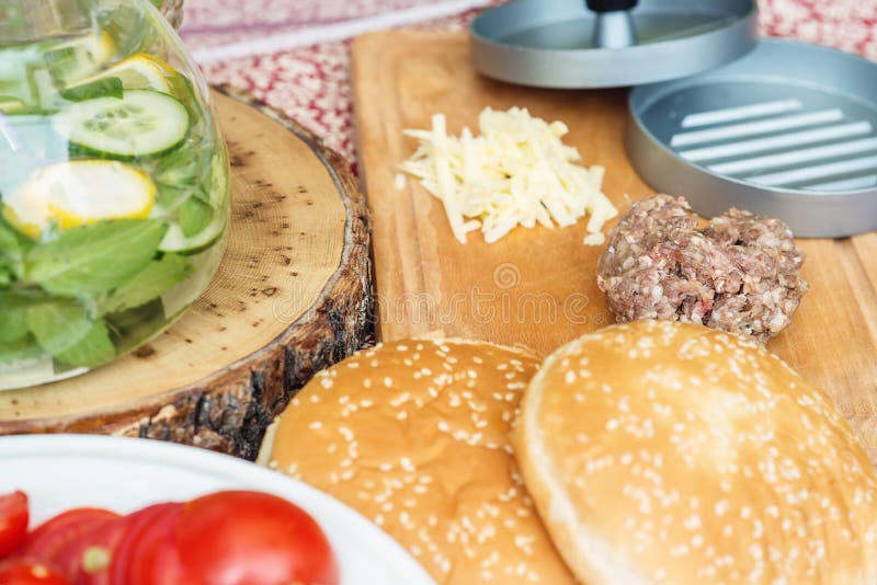 Ingredients for cooking burgers. Raw ground beef meat cutlets on wooden chopping board, red onion, cherry tomatoes, greens, cheese royalty free stock photos Ingredients for cooking burgers. Raw ground beef meat cutlets on wooden chopping board, red onion, cherry tomatoes, greens, cheese royalty free stock photos