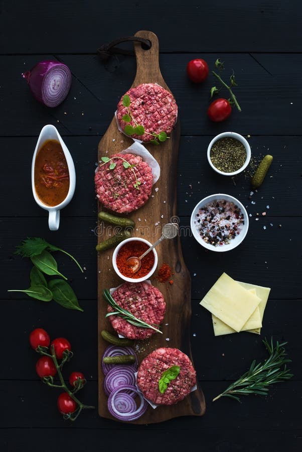 Ingredients for cooking burgers. Raw ground beef meat cutlets on wooden chopping board, red onion, cherry tomatoes royalty free stock image Ingredients for cooking burgers. Raw ground beef meat cutlets on wooden chopping board, red onion, cherry tomatoes royalty free stock image