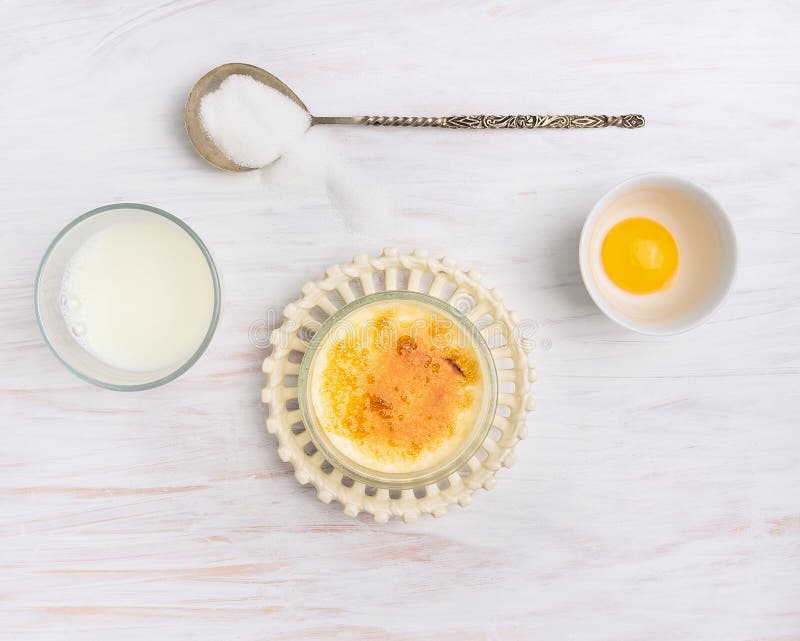 Ingredients for creme brulee : milk, cream, egg yolk , sugar on white wooden background, top view