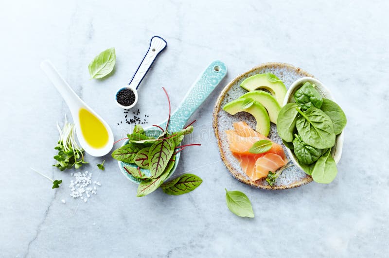 Ingredients for a healthy salad on gray stone background. Smoked salmon, avocado, spinach, sorrel, radis sprouts, black cumin.