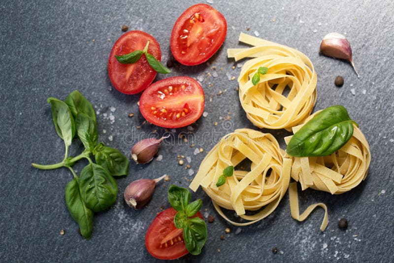 Ingrediënten voor het koken van deegwaren Italiaanse tagliatelledeegwaren met tomaat op zwarte houten achtergrond stock afbeeldingen Ingrediënten voor het koken van deegwaren Italiaanse tagliatelledeegwaren met tomaat op zwarte houten achtergrond stock afbeeldingen