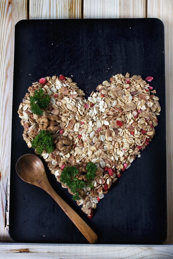Ingrediënten voor het koken van gezond ontbijt in een vorm van hart Noten, havervlokken, droge vruchten, honing, granola royalty-vrije stock foto Ingrediënten voor het koken van gezond ontbijt in een vorm van hart Noten, havervlokken, droge vruchten, honing, granola royalty-vrije stock foto