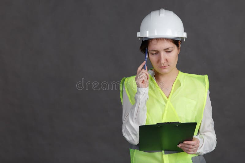 Ingénieur de jeune femme dans le casque de protection et gilet avec le stylo et comprimé dans des mains Pense au-dessus de l'idée photos libres de droits Ingénieur de jeune femme dans le casque de protection et gilet avec le stylo et comprimé dans des mains Pense au-dessus de l'idée photos libres de droits