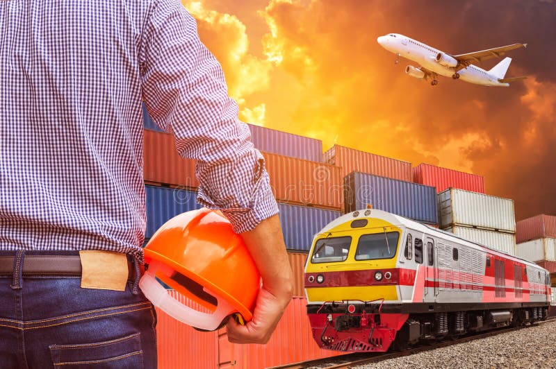 Ingénieur tenant le train de fret commercial fonctionnant jaune de cargaison de contrôle de casque de sécurité avec la pile de ca photo libre de droits Ingénieur tenant le train de fret commercial fonctionnant jaune de cargaison de contrôle de casque de sécurité avec la pile de ca photo libre de droits