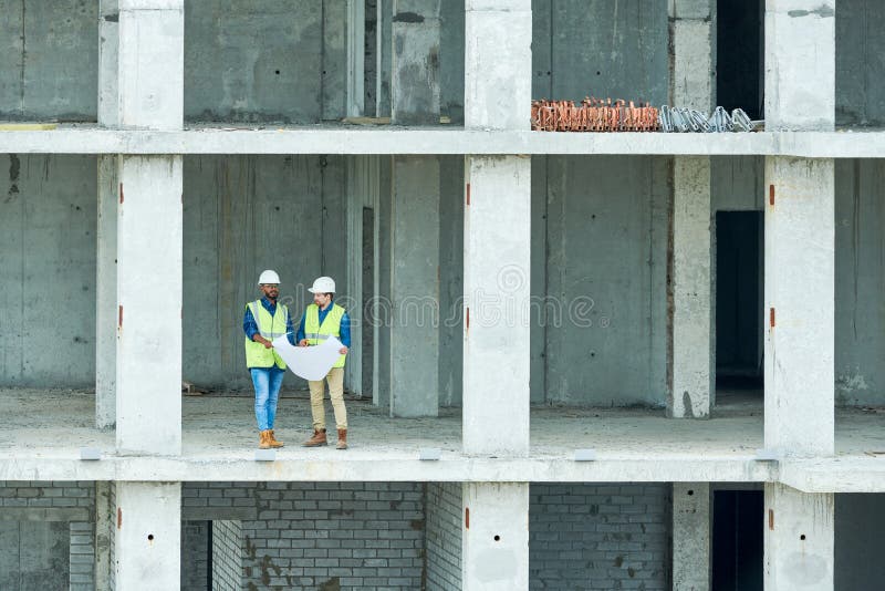 Ingénieurs de construction lisant l'ébauche dans le bâtiment non fini photo libre de droits Ingénieurs de construction lisant l'ébauche dans le bâtiment non fini photo libre de droits