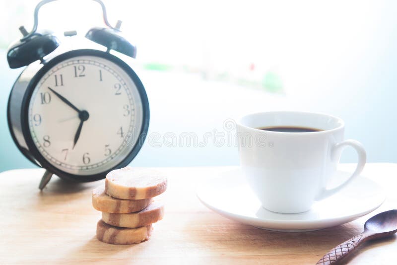 Inizi sul concetto con la tazza di caffè, i biscotti e la sveglia fotografia stock libera da diritti Inizi sul concetto con la tazza di caffè, i biscotti e la sveglia fotografia stock libera da diritti