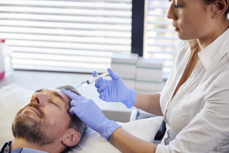 Injection femelle de Botox de patient de Giving Mature Male d'esthéticien dans le front photos libres de droits Injection femelle de Botox de patient de Giving Mature Male d'esthéticien dans le front photos libres de droits