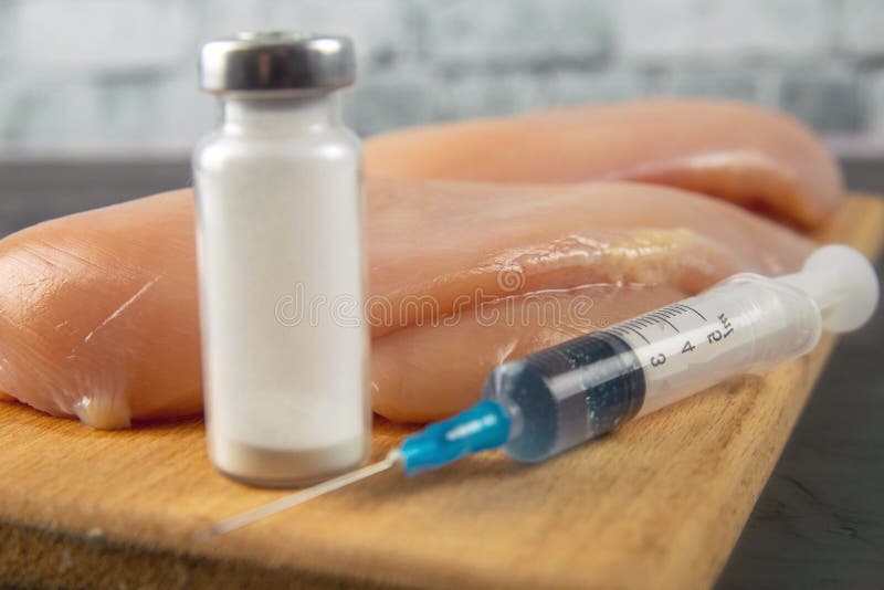 Injection syringe in raw chicken pieces, concept of injection of GMOs into the meat. Close-up