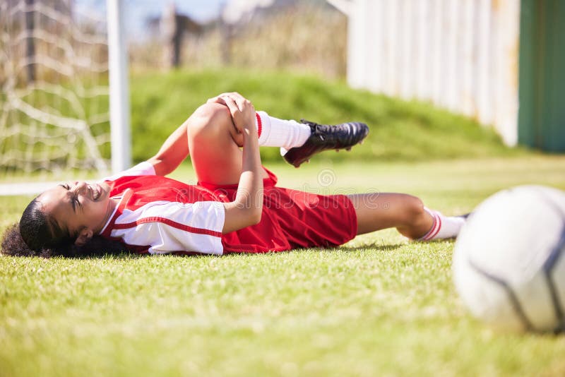 Injured, pain or injury of a female soccer player lying on a field holding her knee during a match. Hurt woman
