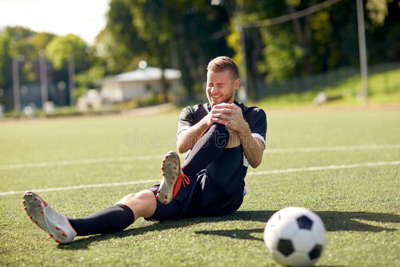 Sport, football training, sports injury and people - injured soccer player with ball on field. Sport, football training, sports injury and people - injured soccer player with ball on field