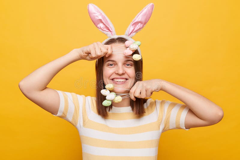 Inquadratura orizzontale di una donna allegra e soddisfatta, con le orecchie di coniglio che tiene in mano le torte di Pasqua, iso immagine stock