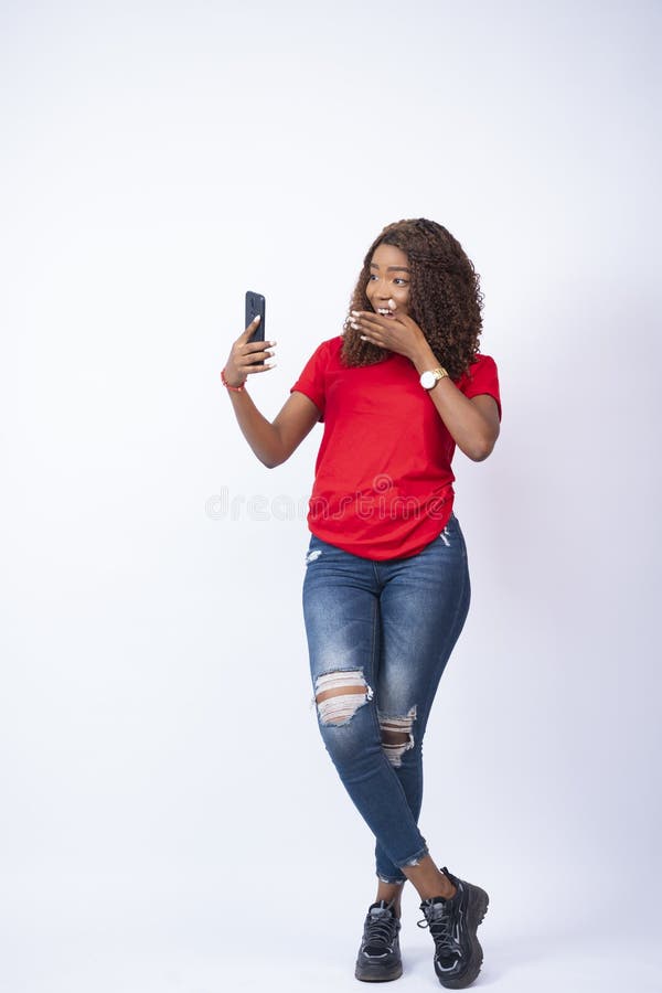 Inquadratura verticale di una bellissima donna nera che si sente sorpresa mentre guarda il suo telefono fotografia stock libera da diritti