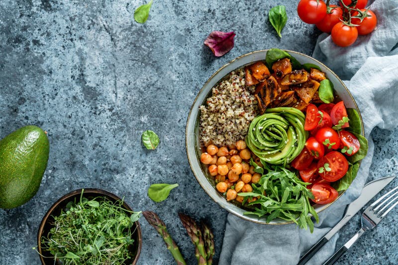 Buddha bowl salad with baked sweet potatoes, chickpeas, quinoa, tomatoes, arugula, avocado, sprouts on light blue background with napkin. Healthy vegan food, clean eating, dieting, top view. Buddha bowl salad with baked sweet potatoes, chickpeas, quinoa, tomatoes, arugula, avocado, sprouts on light blue background with napkin. Healthy vegan food, clean eating, dieting, top view