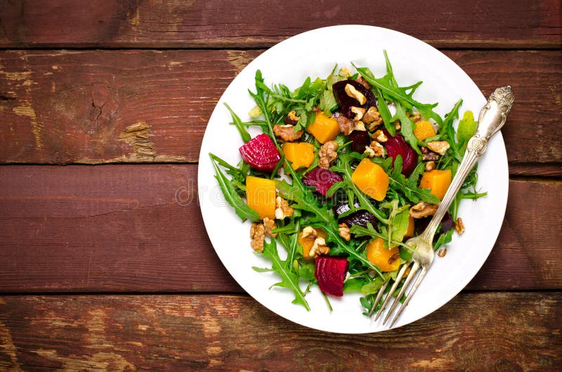 Insalata di caduta con i verdi, rucola, noci, barbabietola e zucca arrostita, zucca su fondo di legno fotografie stock libere da diritti Insalata di caduta con i verdi, rucola, noci, barbabietola e zucca arrostita, zucca su fondo di legno fotografie stock libere da diritti