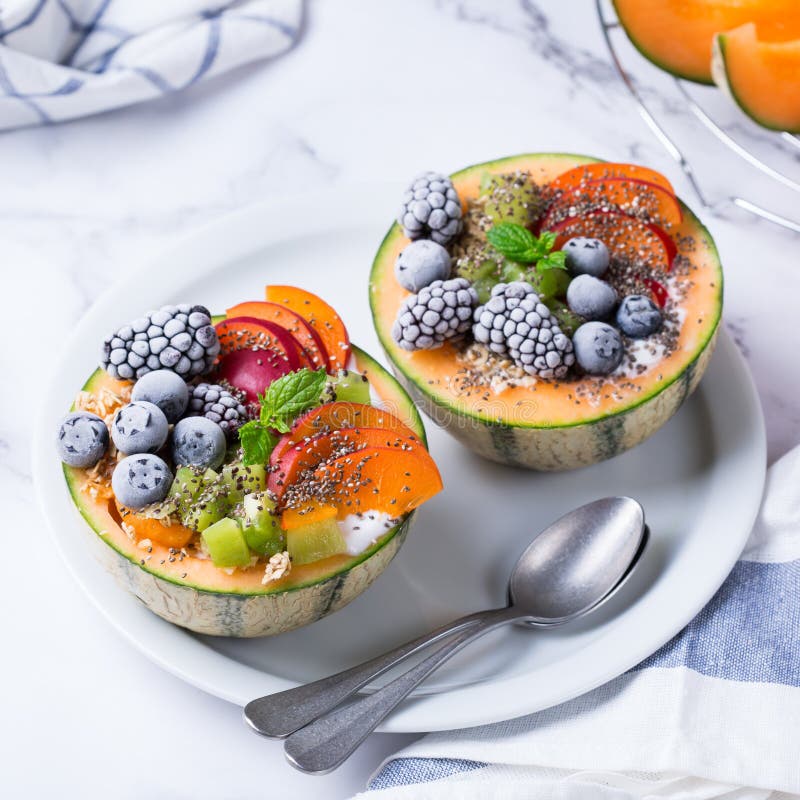 Healthy clean eating, dieting and nutrition, seasonal, summer breakfast concept. Fruit salad with yogurt in carved melon cantaloupe bowl on a kitchen table. Healthy clean eating, dieting and nutrition, seasonal, summer breakfast concept. Fruit salad with yogurt in carved melon cantaloupe bowl on a kitchen table