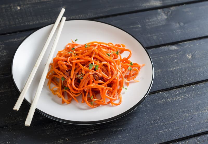 Insalata marinata piccante della carota in uno stile asiatico su un piatto bianco su un fondo di legno scuro fotografie stock libere da diritti Insalata marinata piccante della carota in uno stile asiatico su un piatto bianco su un fondo di legno scuro fotografie stock libere da diritti