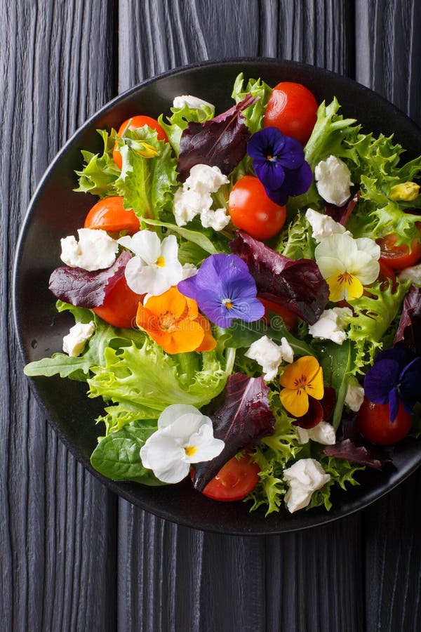 Insalata mista dei fiori commestibili con lattuga, i pomodori e la crema c. Insalata mista dei fiori commestibili con il primo piano del pomodoro e del formaggio cremoso della lattuga, sulla tavola Vista superiore verticale da sopra