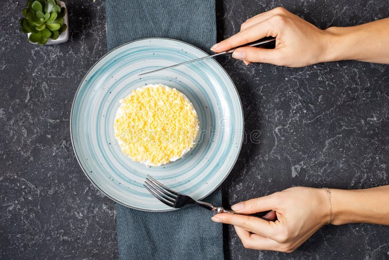 Insalata russa tradizionale Mimosa sulla tavola di pietra Le maniglie femmine tengono il coltello e la forchetta Vista dall'alto immagine stock Insalata russa tradizionale Mimosa sulla tavola di pietra Le maniglie femmine tengono il coltello e la forchetta Vista dall'alto immagine stock