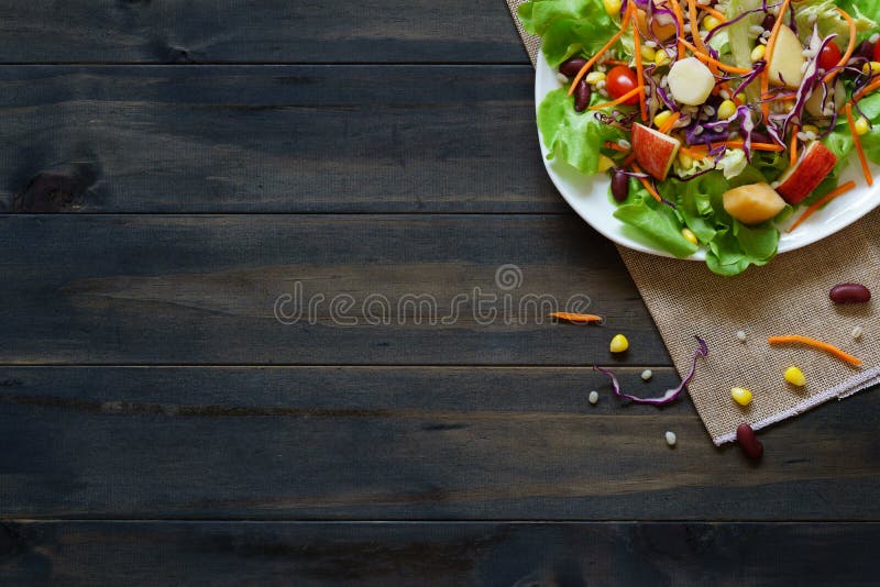 Insalata sana fresca sul piatto bianco con le verdure miste di verdi, il cereale, la carota, il cereale, il perno ed i fagioli rossi sulla vista superiore del fondo di legno con lo spazio della copia Alimento sano