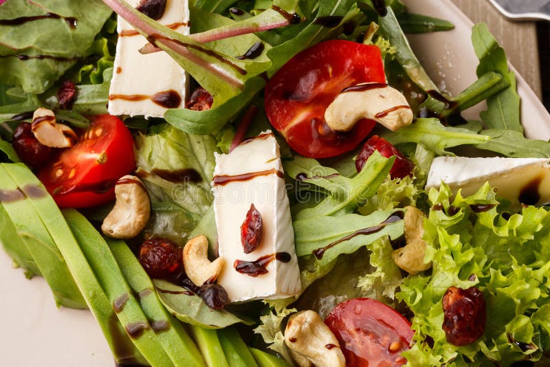 Insalata saporita e sana con la rucola, il brie, il formaggio, l'avocado, i pomodori ciliegia, il mirtillo rosso asciutto e gli a fotografia stock Insalata saporita e sana con la rucola, il brie, il formaggio, l'avocado, i pomodori ciliegia, il mirtillo rosso asciutto e gli a fotografia stock