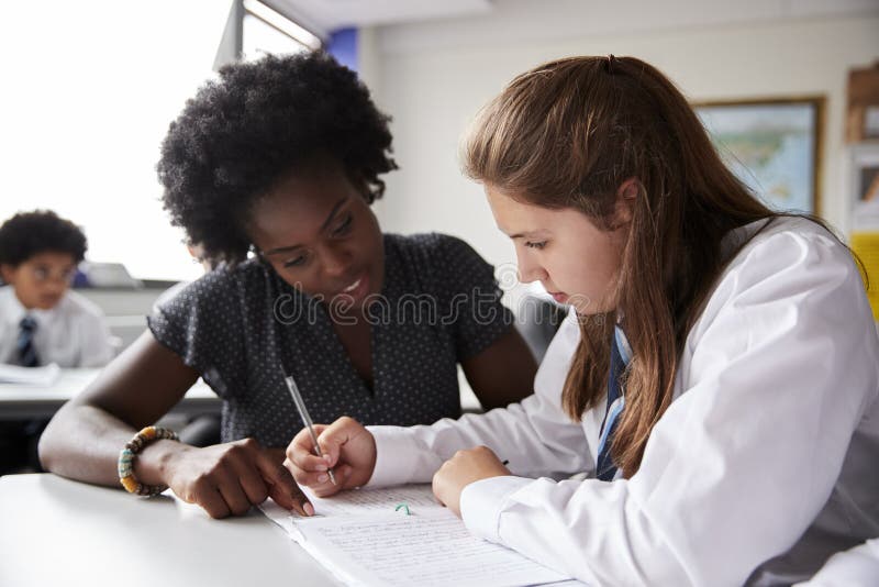 Insegnamento d'uso delle uniformi una - una di Giving Female Student dell'istitutore della High School allo scrittorio immagini stock Insegnamento d'uso delle uniformi una - una di Giving Female Student dell'istitutore della High School allo scrittorio immagini stock