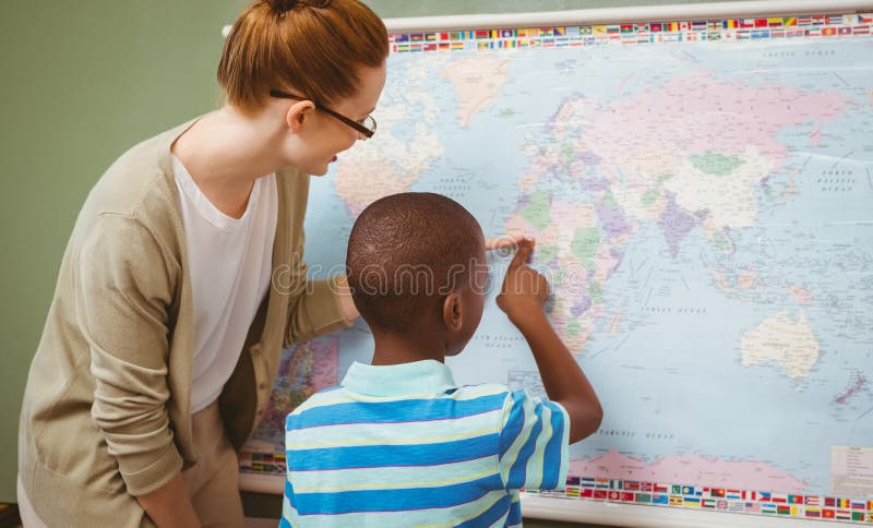 Insegnante che assiste ragazzo per leggere mappa in aula fotografia stock Insegnante che assiste ragazzo per leggere mappa in aula fotografia stock