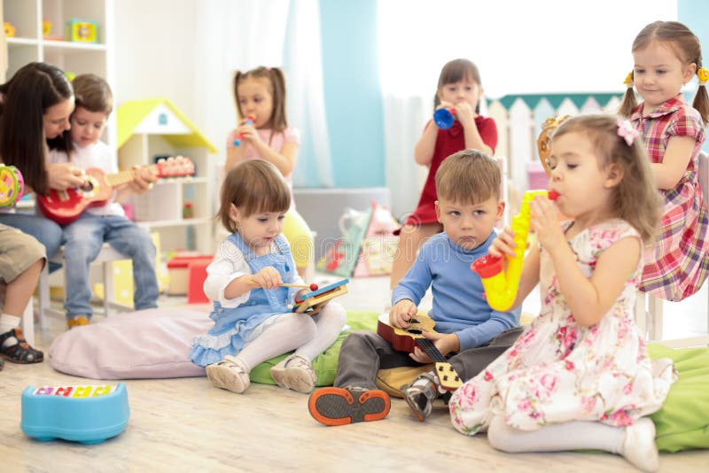 Insegnante e bambini svegli durante la lezione di musica in scuola materna immagine stock Insegnante e bambini svegli durante la lezione di musica in scuola materna immagine stock