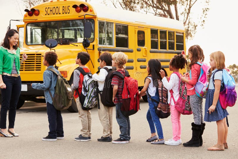 Insegnante e un gruppo di bambini della scuola elementare ad una fermata dell'autobus