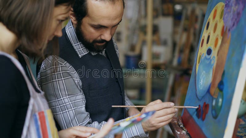 Skilled artist teacher showing and discussing basics of painting to student at art-class indoors. Skilled artist teacher showing and discussing basics of painting to student at art-class indoors