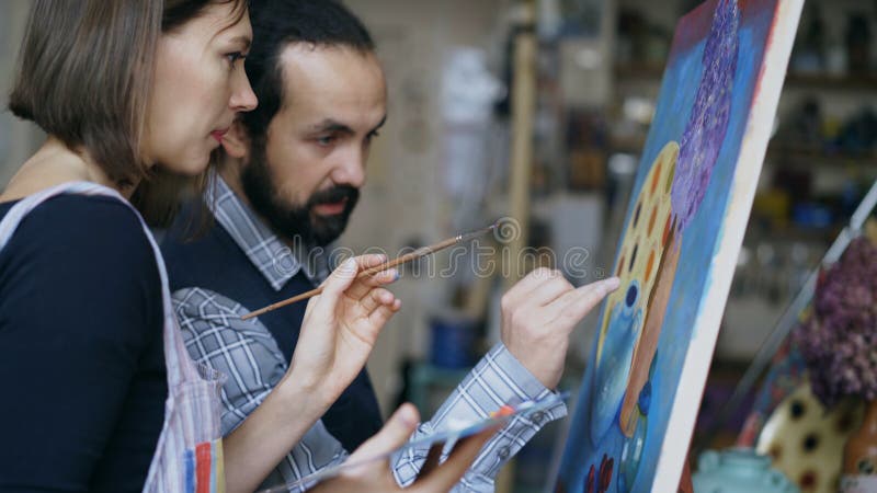 Skilled artist teacher showing and discussing basics of painting to student at art-class indoors. Skilled artist teacher showing and discussing basics of painting to student at art-class indoors