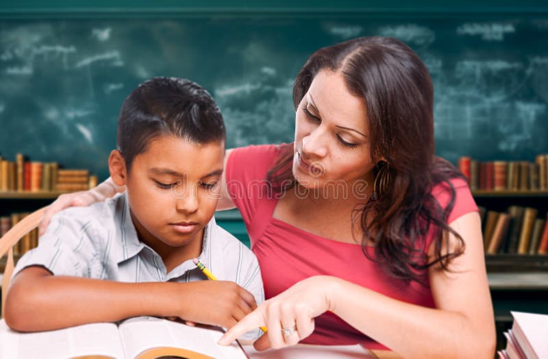 Insegnante latina che insegna a un giovane ispanico nella biblioteca scolastica immagini stock