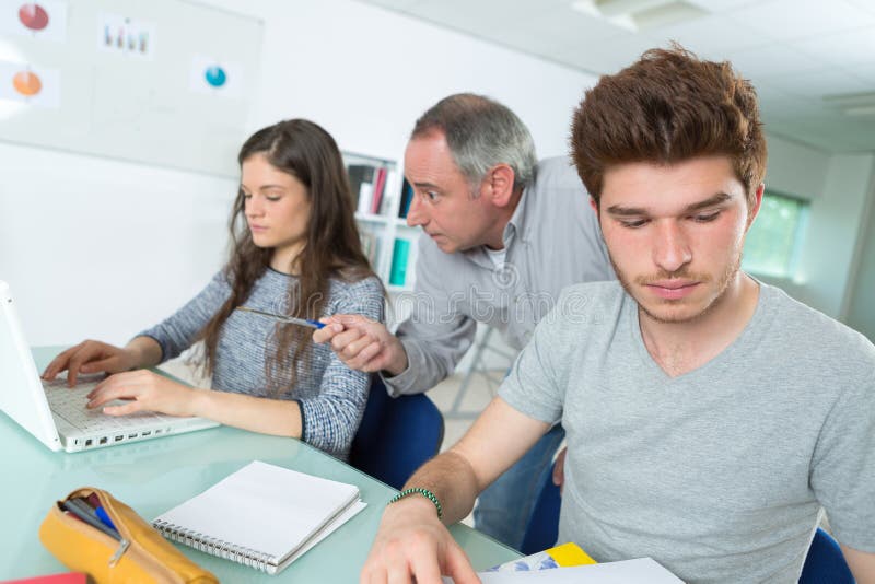 Insegnante o istitutore con gli studenti in aula con il computer portatile fotografia stock Insegnante o istitutore con gli studenti in aula con il computer portatile fotografia stock