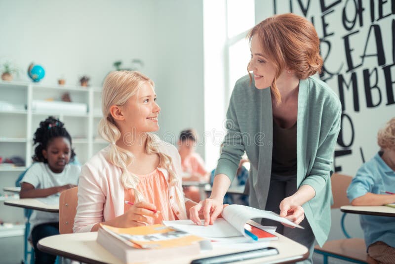 Insegnante sorridente che spiega il compito ad una ragazza della scuola fotografia stock Insegnante sorridente che spiega il compito ad una ragazza della scuola fotografia stock