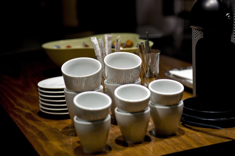 Stacked coffee cups in a shop with plates and coffee machine, image taken on dark only with the focus on the cups as main detail. Stacked coffee cups in a shop with plates and coffee machine, image taken on dark only with the focus on the cups as main detail