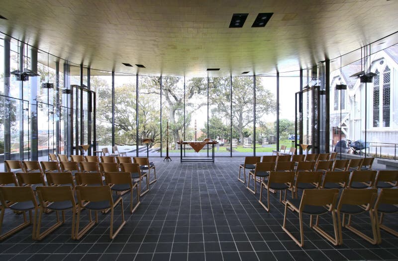 Inside contemporary church with rows of wooden seating. Indoor religious architecture with array of wood chairs. House of worship. Christian assembly hall. Inside contemporary church with rows of wooden seating. Indoor religious architecture with array of wood chairs. House of worship. Christian assembly hall.