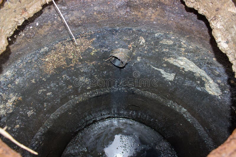 Inside drainage pit,dangerously open drainage pit with dirt and black swamp with water stock photography