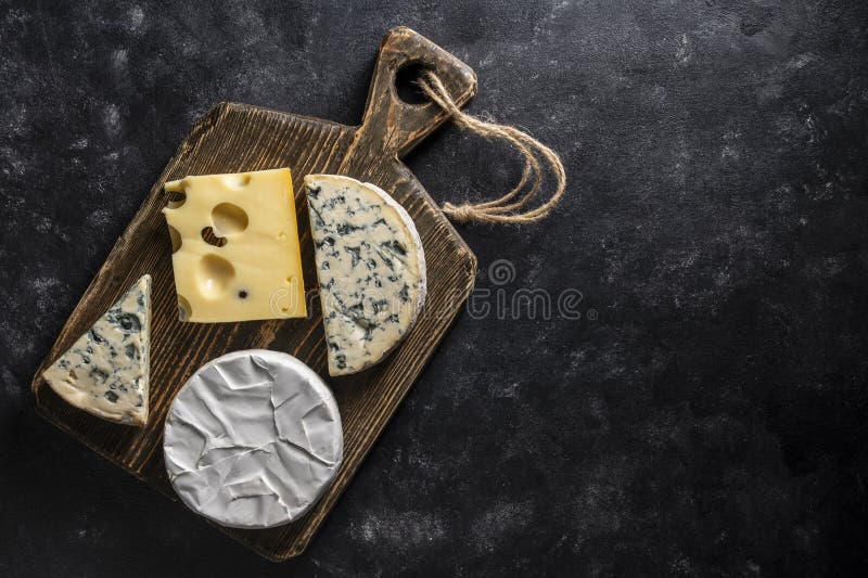 Insieme di formaggi diversi su tavolette di legno su uno spazio di chiusura in alto di fondo nero. Vari tipi di formaggio fotografia stock