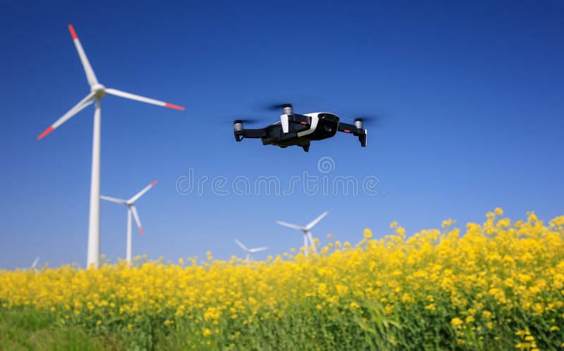 Inspection drone with eolian turbines behind. Rapeseed field in bloom. Renewable energy stock photo Inspection drone with eolian turbines behind. Rapeseed field in bloom. Renewable energy stock photo