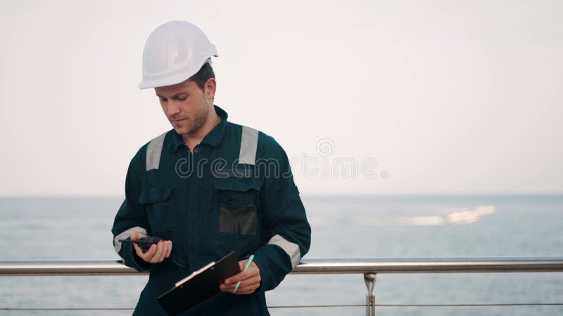 Inspector de puertos de la estación marítima con portapapeles y radio vhf haciendo notas en la lista de verificación