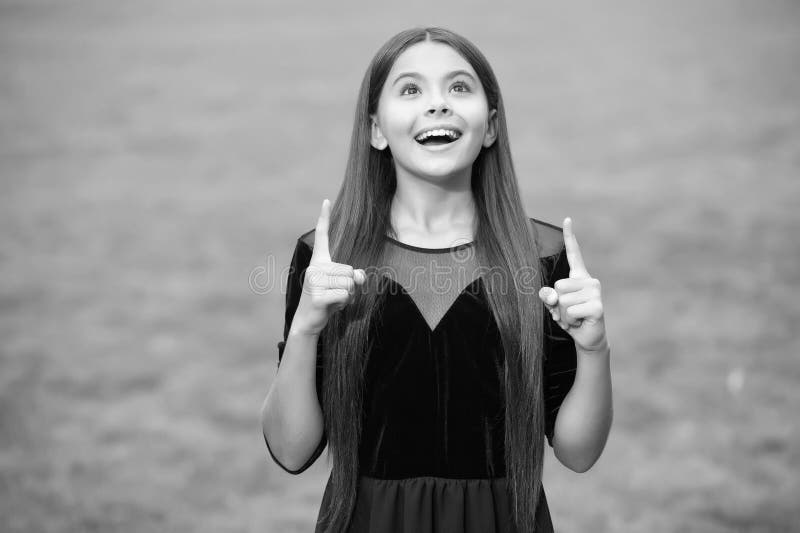 Inspirada niña feliz con el pelo largo vestido de moda buscar manteniendo dedos indeex levantados pasto verde verano al aire libre imagen de archivo