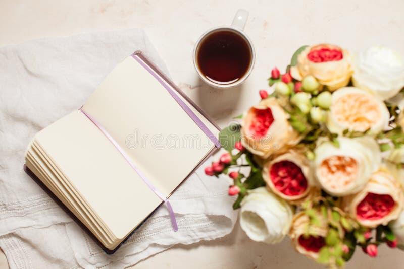 A cup of black tea, notebook and beautiful flowers on the table, top view. The concept of inspiration to creativity. A cup of black tea, notebook and beautiful flowers on the table, top view. The concept of inspiration to creativity