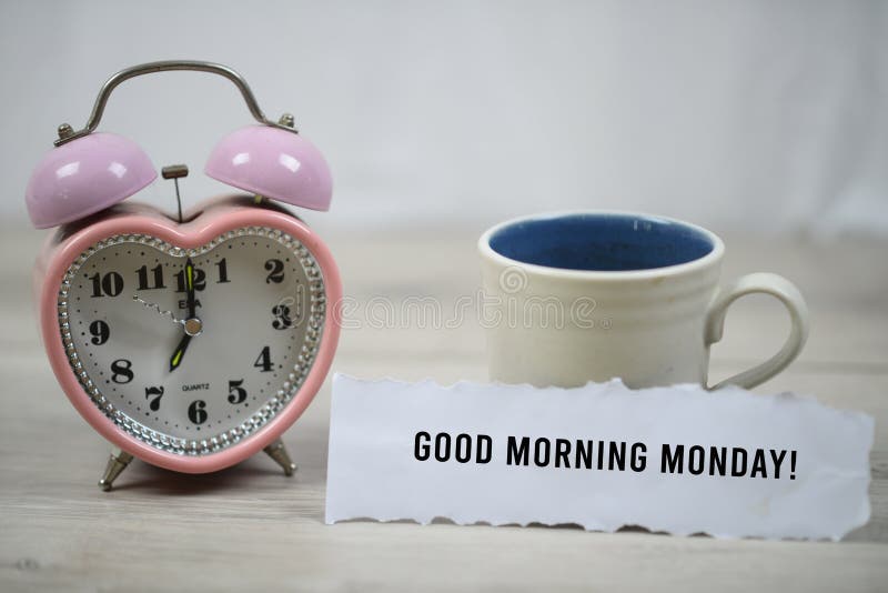Inspirational quote - Good morning Monday. With pink desk clock and a white mug of coffee on wooden white table background. Greeting motivational words concept