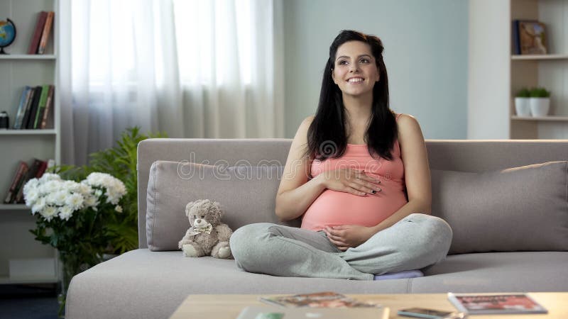 Inspired pregnant lady stroking tummy, dreaming of soonest appearance of newborn