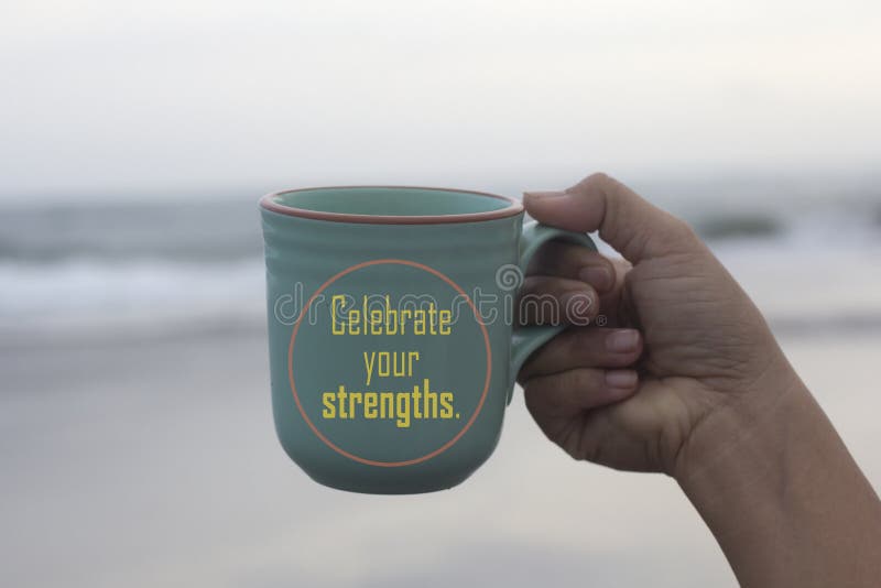 Inspirational text message on a coffee cup - Celebrate your strengths. With person holding a cup of coffee in hand on white misty morning beach background. Self love care and celebrating life concept. Inspirational text message on a coffee cup - Celebrate your strengths. With person holding a cup of coffee in hand on white misty morning beach background. Self love care and celebrating life concept